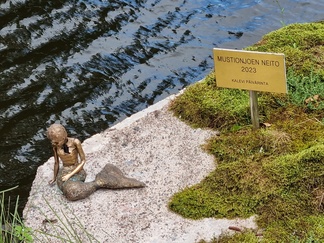 Pieni merenneitopatsas joen ylittävällä sillalla; "Mustionjoen Neito 2023", tekijä Kalevi Päivärinta